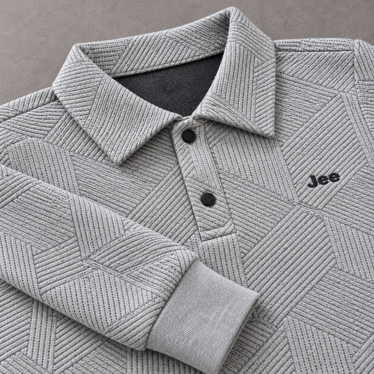 Close-up of raised geometric knit texture, two-button polo collar, Jee logo and ribbed sleeve cuff